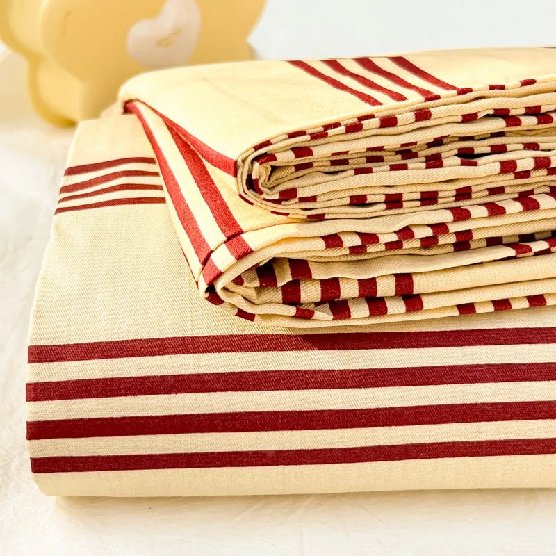 A stack of beige and red striped organic cotton bedding, including a flat sheet and pillowcases.