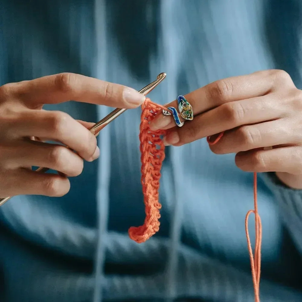 Hands are using a crochet hook to manipulate colorful tension rings for knitting.