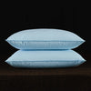 Two light blue natural goose down and feather sleeping pillows resting on a dark surface.