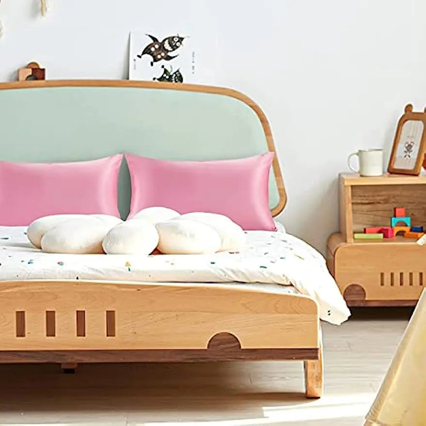 A wooden bed with pink pillows and a light green headboard, featuring silky satin toddler pillowcases.