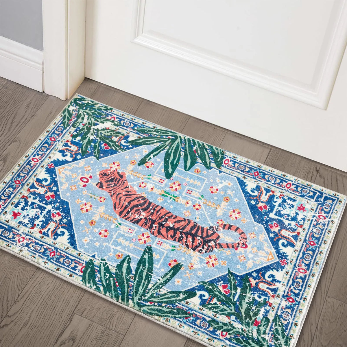 A rectangular entryway rug featuring a blue and white pattern with pink tiger and tropical palm leaf designs.