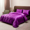 A purple satin luxury bedding set is displayed on a bed with a brown headboard and light curtains.
