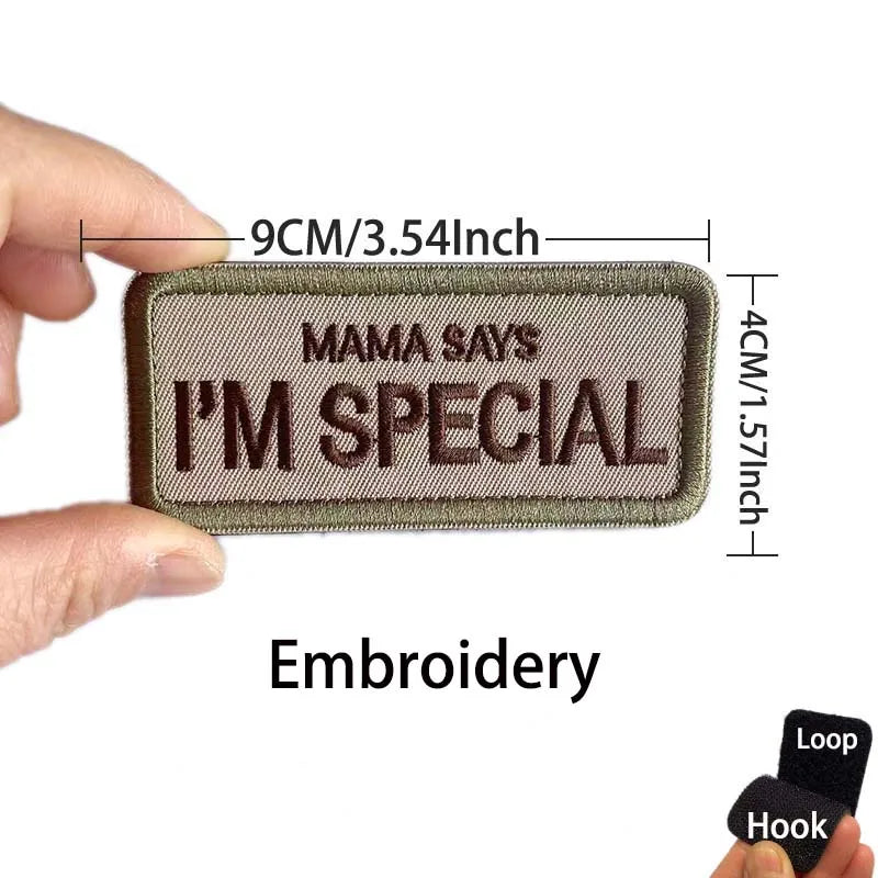 A close-up of a brown embroidered patch that says Mama Says I'm Special, shown being held by a hand.