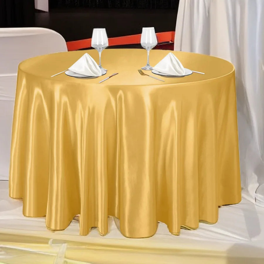 A round table set with a golden satin tablecloth, white napkins, and wine glasses for elegant decor.