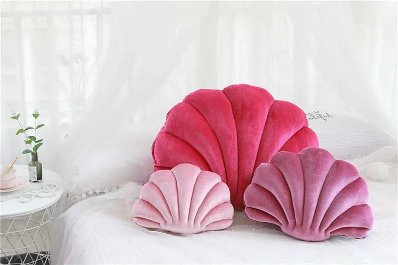 Pink velvet stuffed sofa cushions shaped like decorative seashells on a white bed.