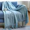 A light blue knitted tassel throw blanket draped over a blue sofa.