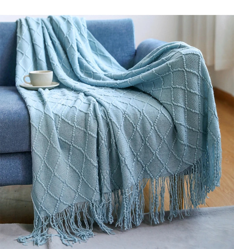 A light blue knitted tassel throw blanket draped over a blue sofa.