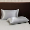 A set of luxury solid satin pillows resting on a light surface against a dark brown headboard.