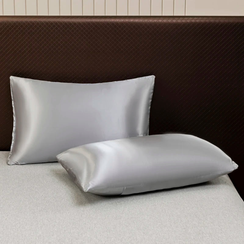 A set of luxury solid satin pillows resting on a light surface against a dark brown headboard.