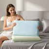 A woman is sitting on a bed with a light blue ice silk cooling pillowcase placed on the sheet.
