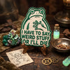 An embroidered patch of a frog saying I have to say weird stuff or I'll die resting on wood and surrounded by natural element