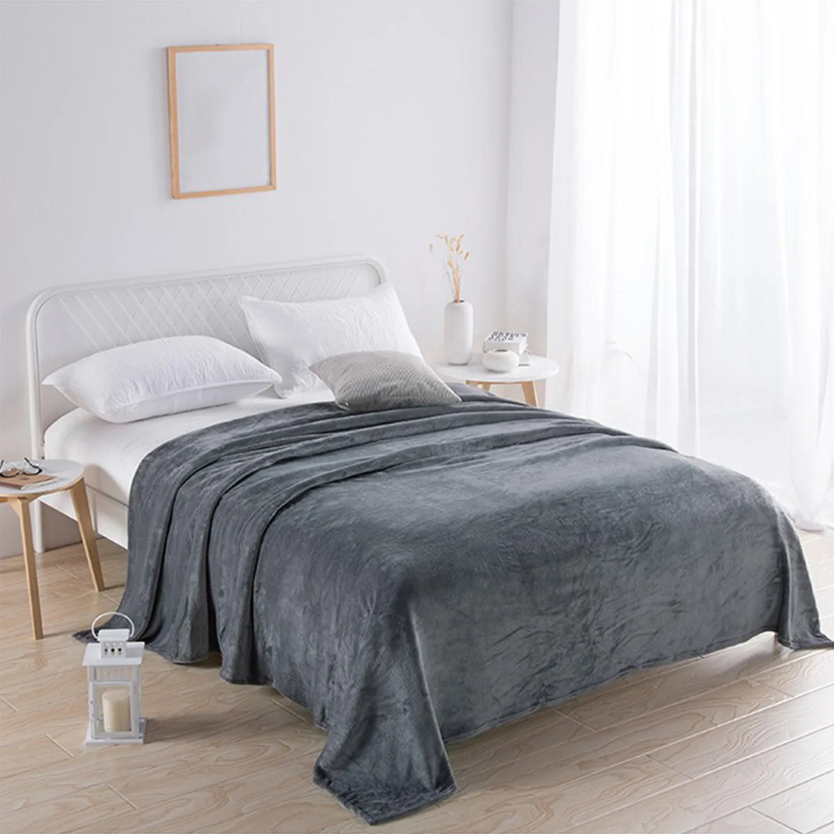 A gray coral fleece throw blanket draped over a white bed in a bright, minimalist bedroom.