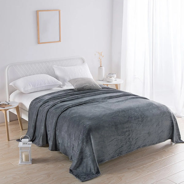 A gray coral fleece throw blanket draped over a white bed in a bright, minimalist bedroom.