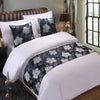 A close-up of a bed with white linens and decorative navy blue and silver floral patterned pillowcases.