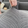 A hand is adjusting the textured gray jacquard stretch sofa cover on a piece of furniture.
