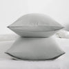 A set of four light gray microfiber pillow covers resting on a white bed.