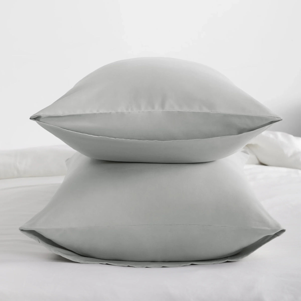 A set of four light gray microfiber pillow covers resting on a white bed.