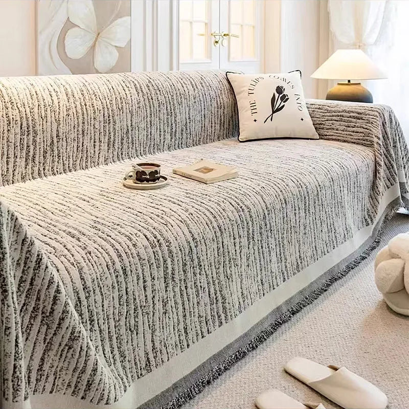 A textured gray jacquard sofa cover blanket draped over a sofa, with a cup and book placed on the fabric.