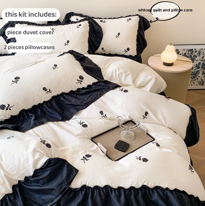 A set of embroidered rose duvet cover and pillowcases in white and navy blue with a matching dark bed skirt.