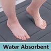 A close-up of a person's foot resting on a dark gray water absorbent memory foam bathroom mat.