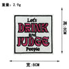 A square embroidered patch with the text Let's DRINK and JUDGE People in pink thread.