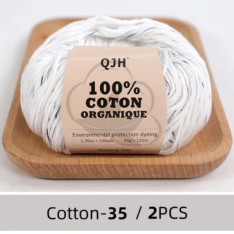 A ball of white organic cotton yarn labeled QJH 100% COTON ORGANIQUE resting on a wooden board.