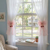 A pair of pink ribbon bow curtain tiebacks framing a window with sheer white drapery.