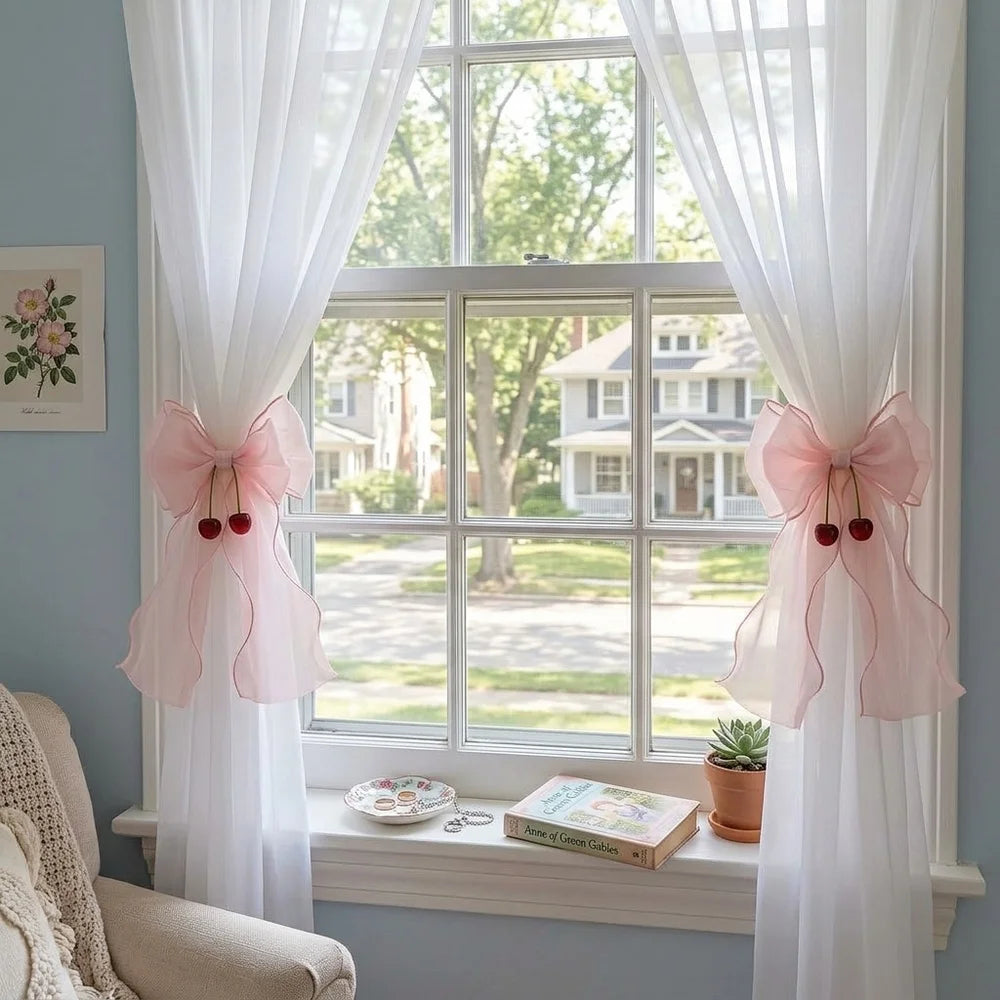A pair of pink ribbon bow curtain tiebacks framing a window with sheer white drapery.
