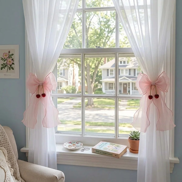 A pair of pink ribbon bow curtain tiebacks framing a window with sheer white drapery.