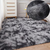 A fluffy gray and black faux fur area rug with a large black decorative pillow on a light wood floor.