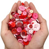 A hand holds a pile of assorted resin sewing buttons in various shades of pink and red.