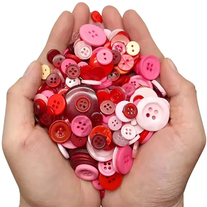 A hand holds a pile of assorted resin sewing buttons in various shades of pink and red.