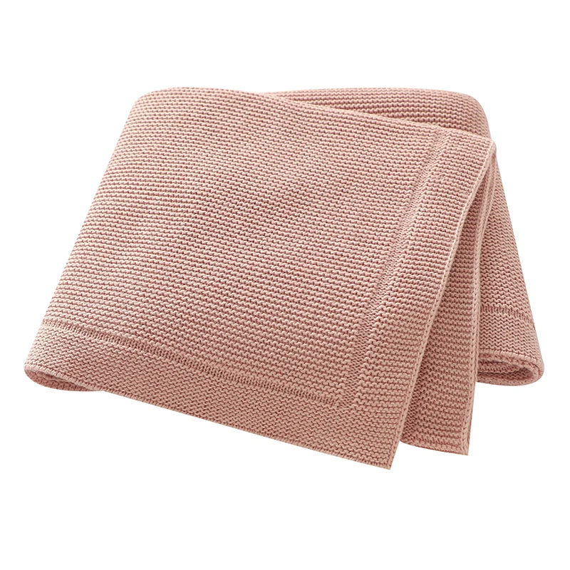 A folded, light pink knitted baby swaddle blanket made of cotton.
