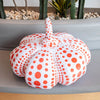 A white pumpkin plush cushion with orange polka dots resting on a gray surface.