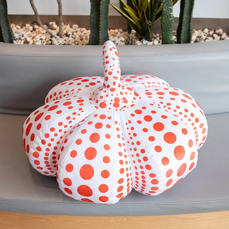 A white pumpkin plush cushion with orange polka dots resting on a gray surface.