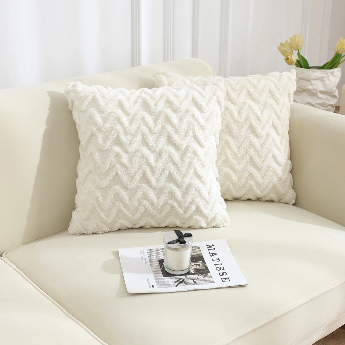 A white jacquard plush throw pillow cover with a geometric chevron pattern resting on a light-colored sofa.