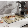 A silver electric coffee grinder and a wooden mat are displayed on a white countertop.