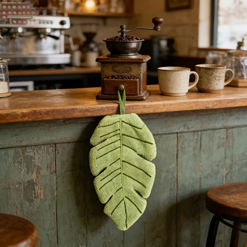 A vibrant green banana leaf hand towel is hanging on a wooden cabinet, displayed in a rustic kitchen setting.