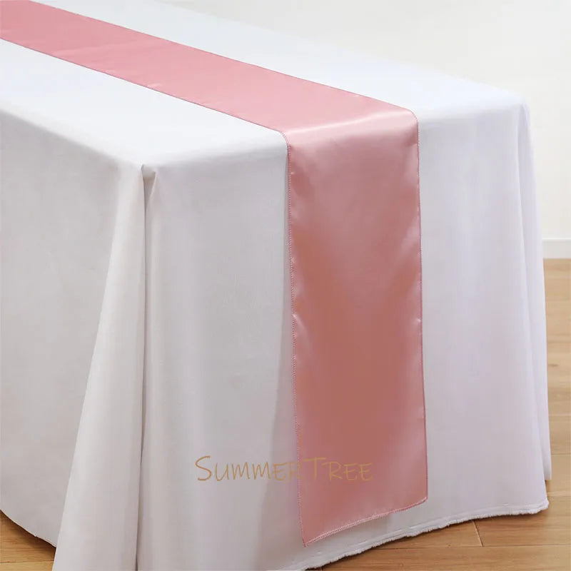 Elegant satin pink table runner draped across a white tablecloth.