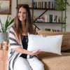 A young woman sits on a couch holding a white throw pillow insert with bounce-back support.