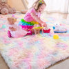 A young girl is playing with stuffed animals on a colorful plush area rug in a bright room.