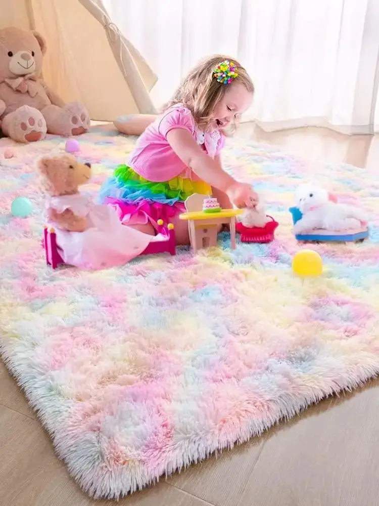 A young girl is playing with stuffed animals on a colorful plush area rug in a bright room.