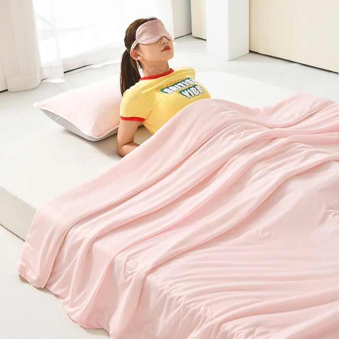 A pink ice silk cooling comforter is draped on a white surface next to a person wearing a yellow shirt and a pink visor.