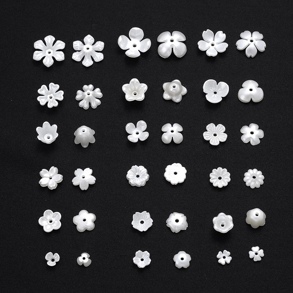 A collection of small white imitation pearl flower spacer beads arranged in rows on a black background.