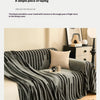A charcoal grey herringbone chenille sofa cover with black and white geometric pattern and tassel fringes draped over a sofa.