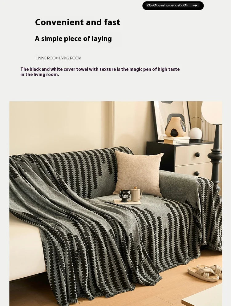 A charcoal grey herringbone chenille sofa cover with black and white geometric pattern and tassel fringes draped over a sofa.