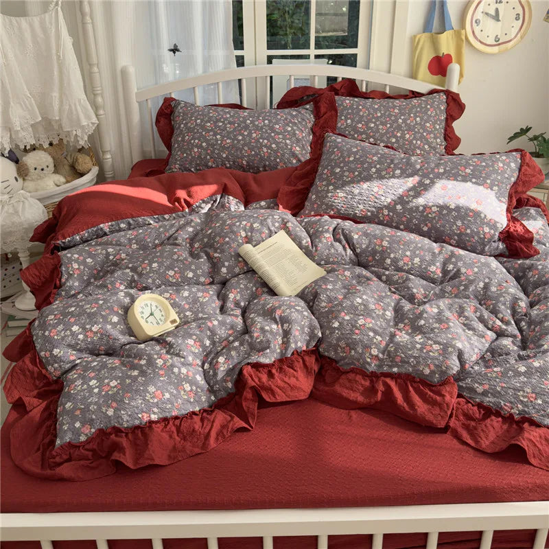 A princess style bedding set featuring a red and gray patterned duvet, pillows, and ruffled bed frame.