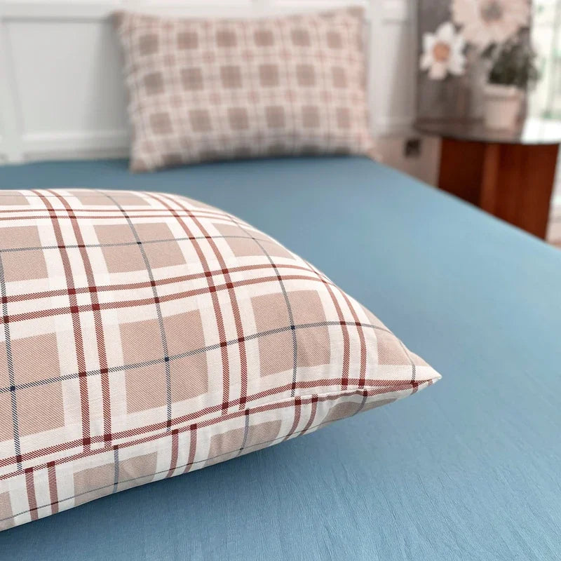 A close-up of a plaid beige and brown patterned pillow resting on a blue bedsheet.