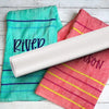 A roll of water-soluble embroidery stabilizer film next to two brightly colored cloths, one teal and one pink.