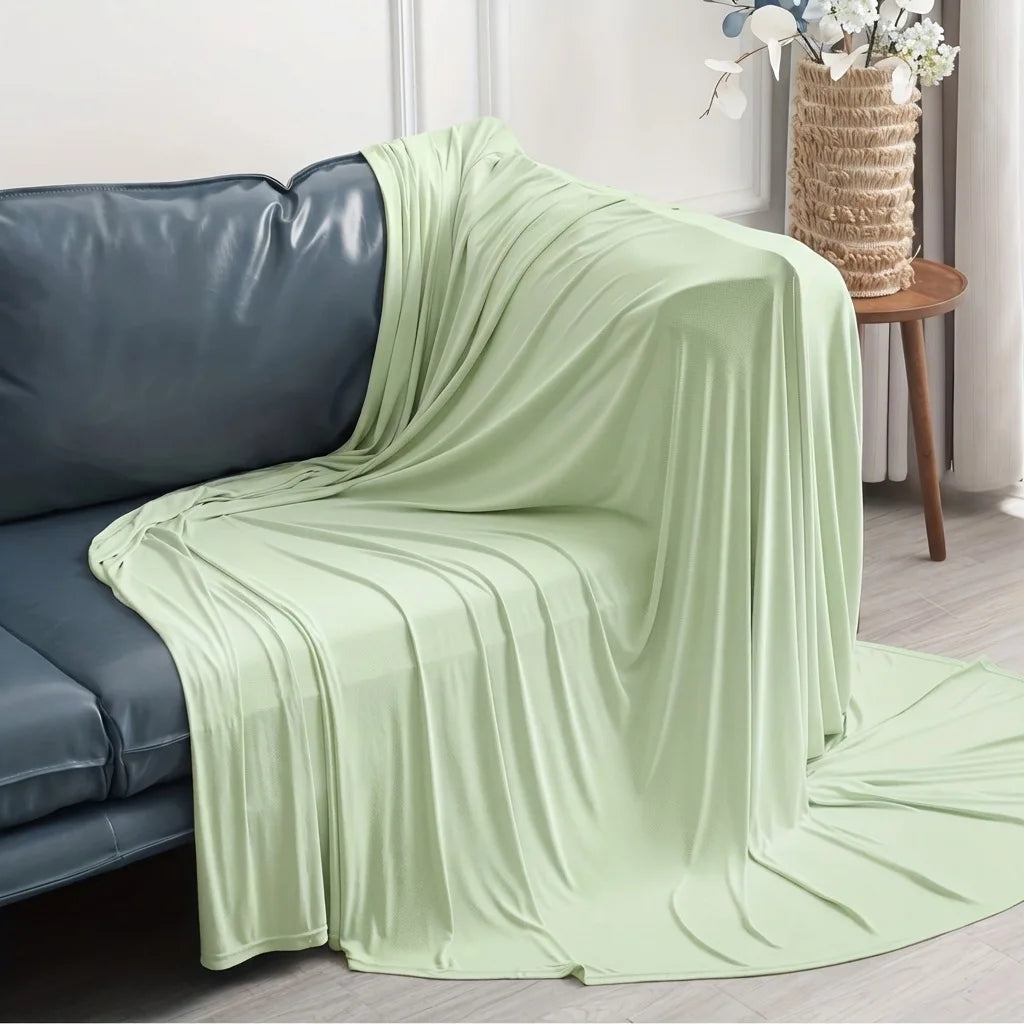 Light green ice silk cooling blanket draped over a dark blue sofa.